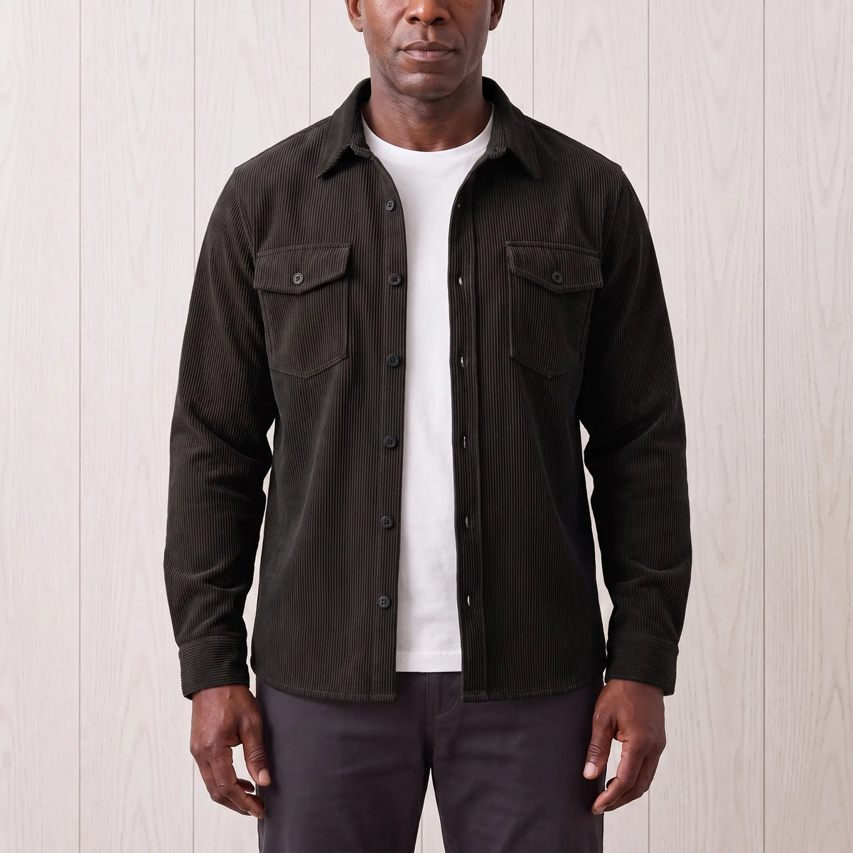 Man wearing the Fine Cord Overshirt in black, a corduroy shirt jacket open over a white tee