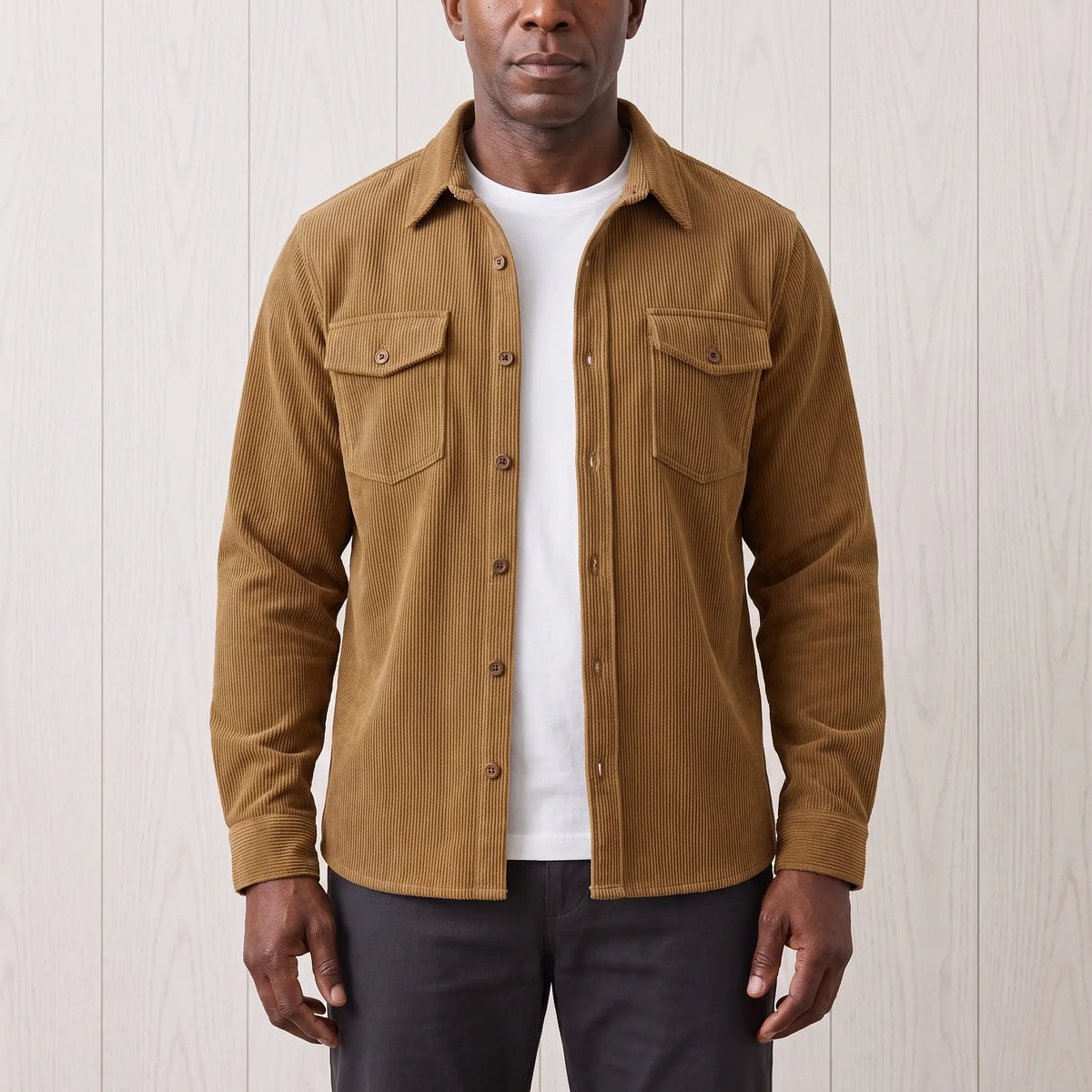 Man wearing the Fine Cord Overshirt in brown, a corduroy shirt jacket with two flap chest pockets, open over a white tee