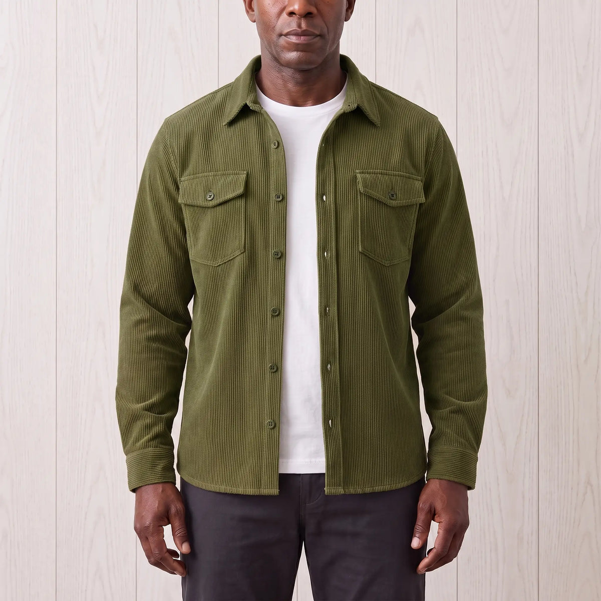 Man wearing the Fine Cord Overshirt in green, an army green corduroy shirt jacket open over a white tee