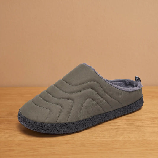 Men's green quilted backless slipper with plush faux-fur lining and speckled sole on an oak floor