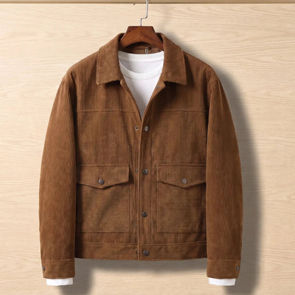 Brown corduroy flap pocket jacket on a wooden hanger against a light oak wall