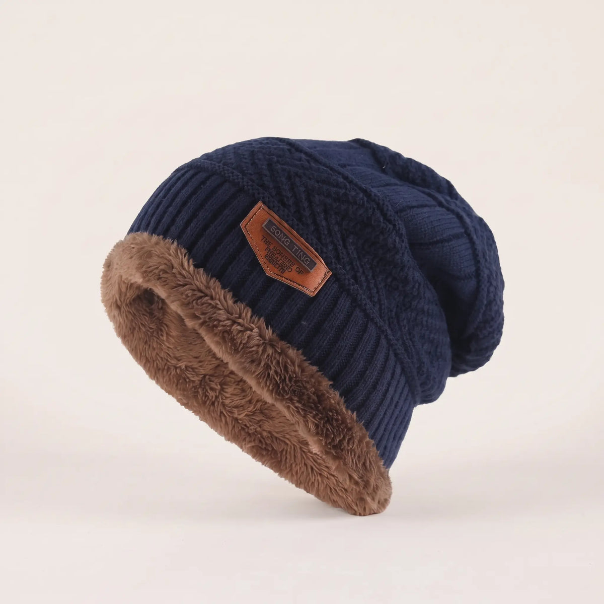 Men's navy blue fleece-lined slouch beanie with textured knit, brown fleece cuff and leather patch