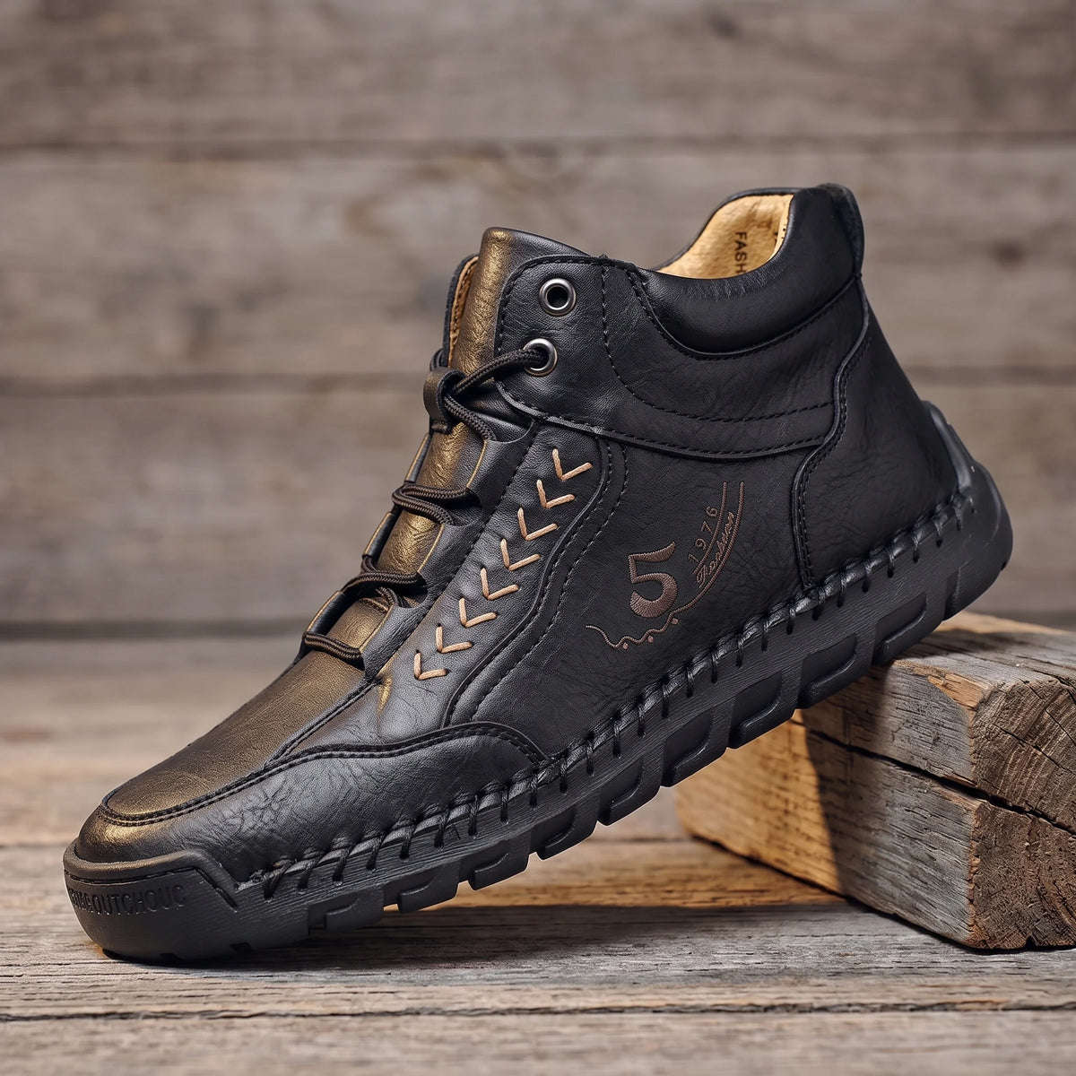 Black hand-stitched leather lace-up ankle boot with flexible rubber sole, side view on reclaimed oak