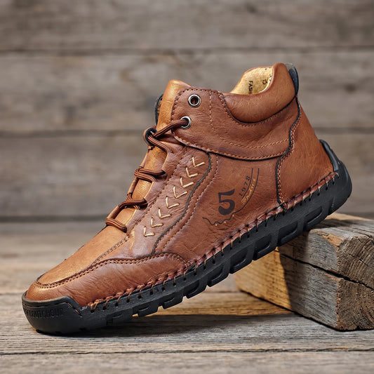 Brown hand-stitched leather lace-up ankle boot with flexible rubber sole, side view on reclaimed oak