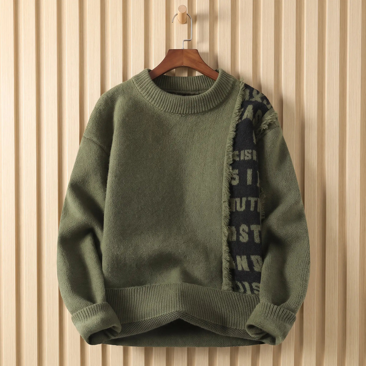 Men's green crew-neck knit sweater with a frayed black lettered panel down the chest, on a wooden hanger