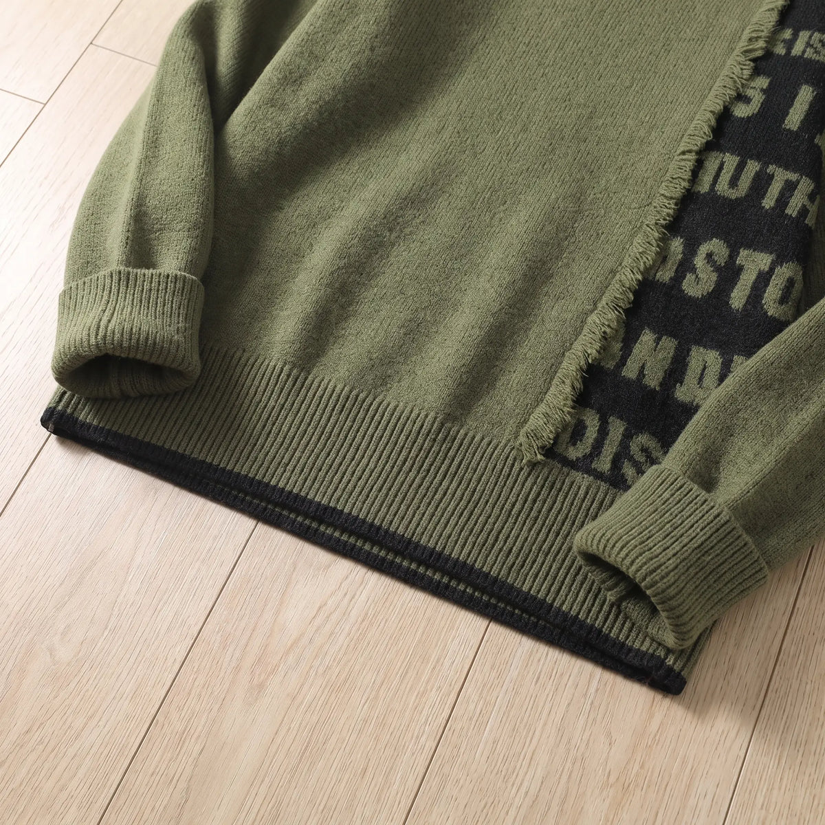 Close-up of the green frayed panel knit layered hem and ribbed cuff
