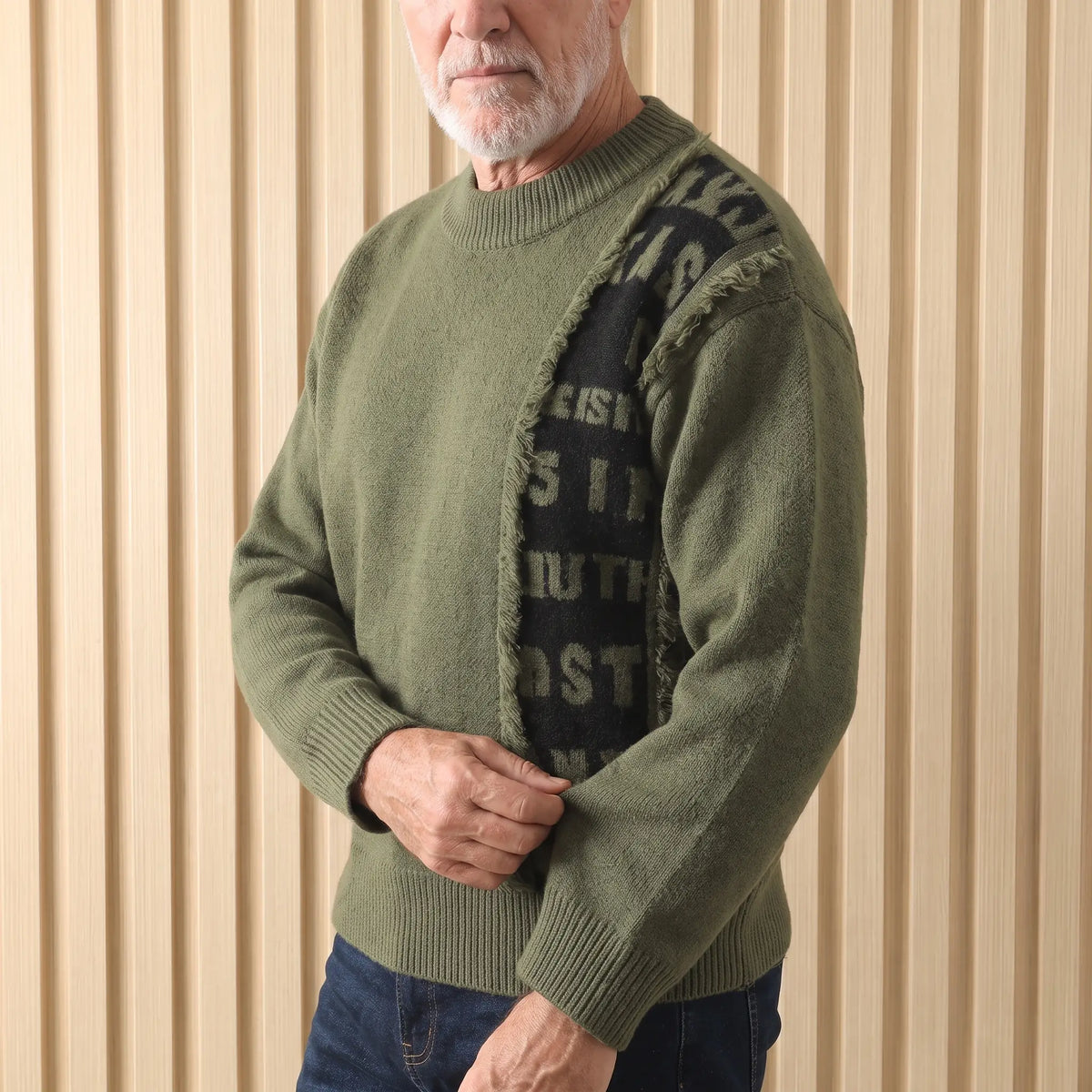 Man wearing the green frayed panel knit sweater, adjusting the cuff