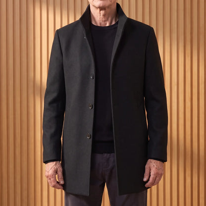 Black funnel neck wool overcoat worn open over a black tee by an older man