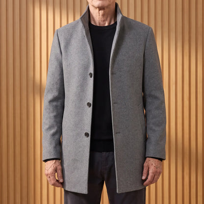 Grey funnel neck wool overcoat worn open over a black tee by an older man