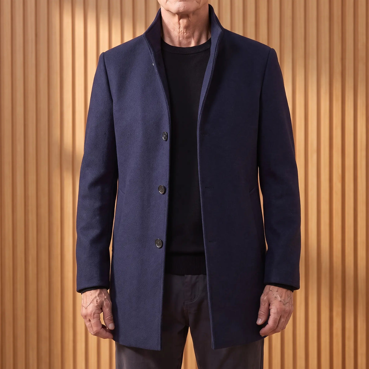 Navy funnel neck wool overcoat worn open over a black tee by an older man