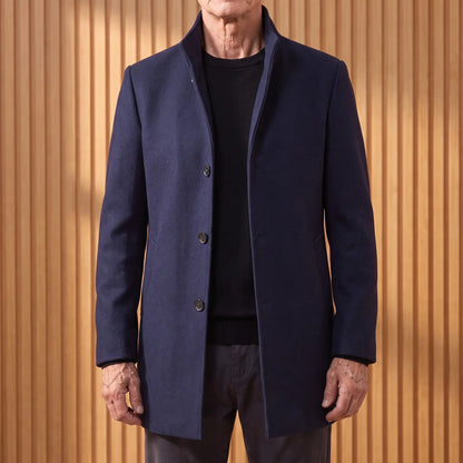 Navy funnel neck wool overcoat worn open over a black tee by an older man