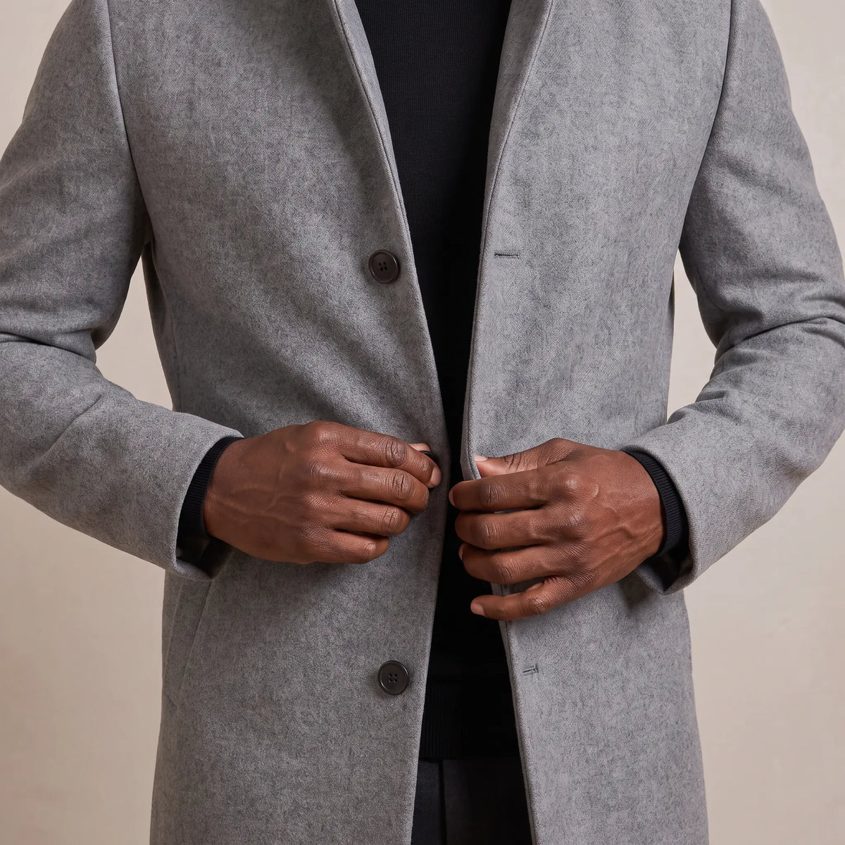Fastening the middle button of the grey wool overcoat