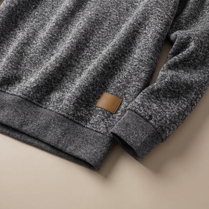 Close-up of the dark grey heather knit sweater ribbed cuff, hem band and leather-look patch