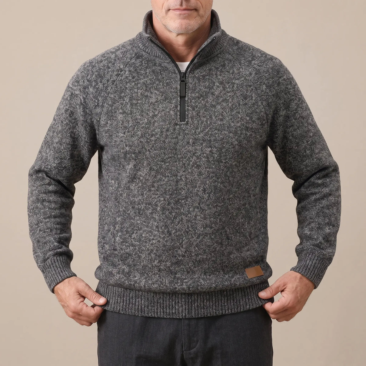Man wearing the dark grey heather knit sweater, straightening the ribbed hem over dark trousers