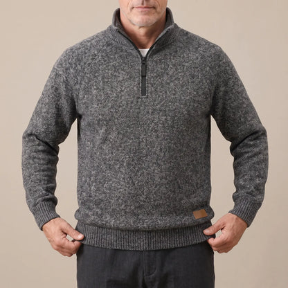 Man wearing the dark grey heather knit sweater, straightening the ribbed hem over dark trousers