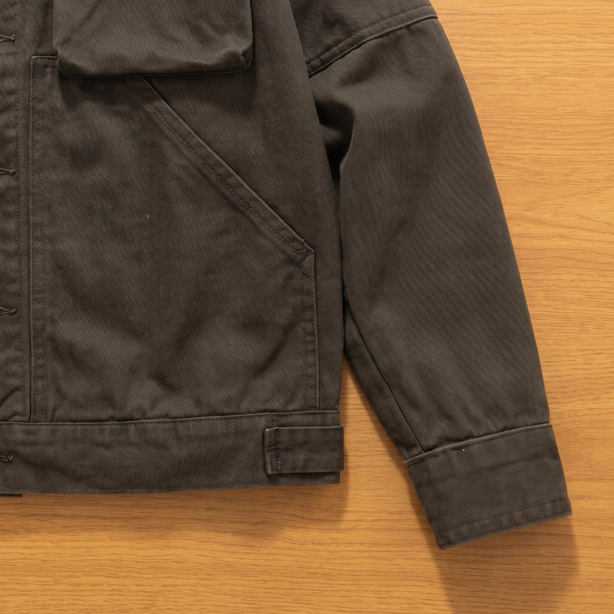 Close up of the slash hand pocket, hem adjuster tab and buttoned cuff on the army green trucker jacket