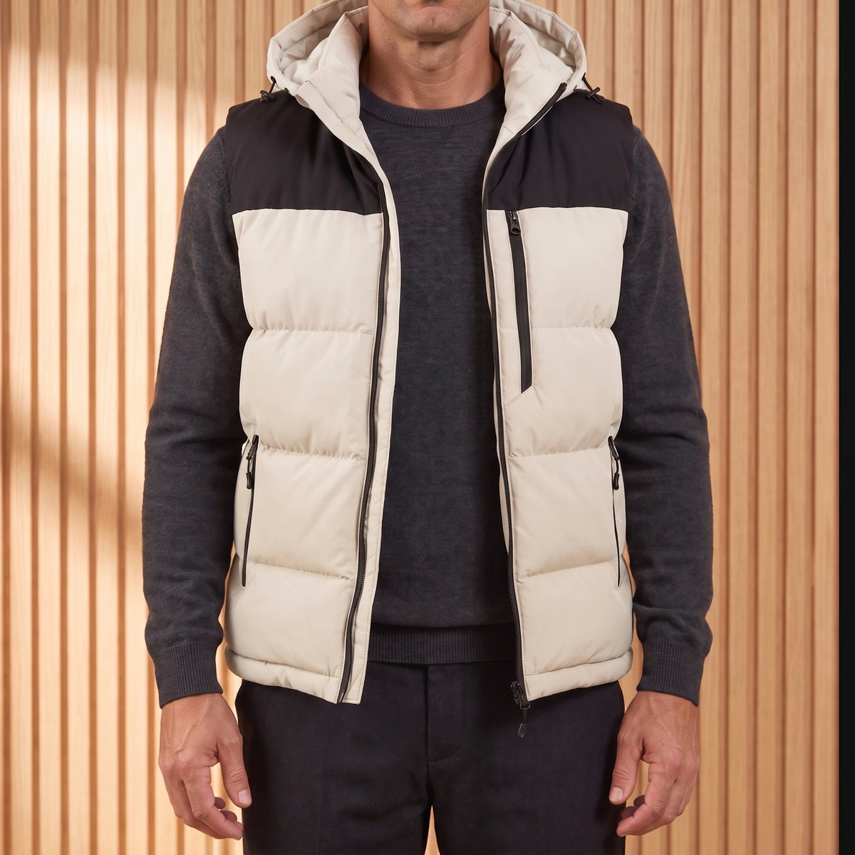 Men's cream hooded puffer vest with black yoke, worn open over a charcoal knit