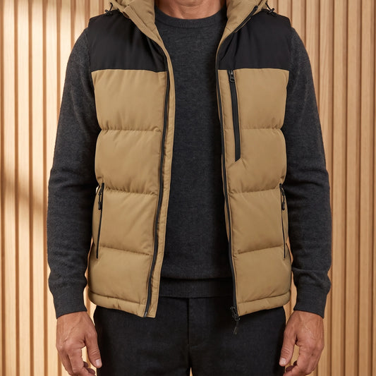 Men's tan hooded puffer vest with black yoke, worn open over a charcoal knit