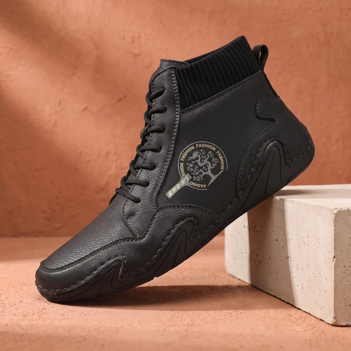 Men's black stitched leather ankle boot with knit collar on a concrete plinth
