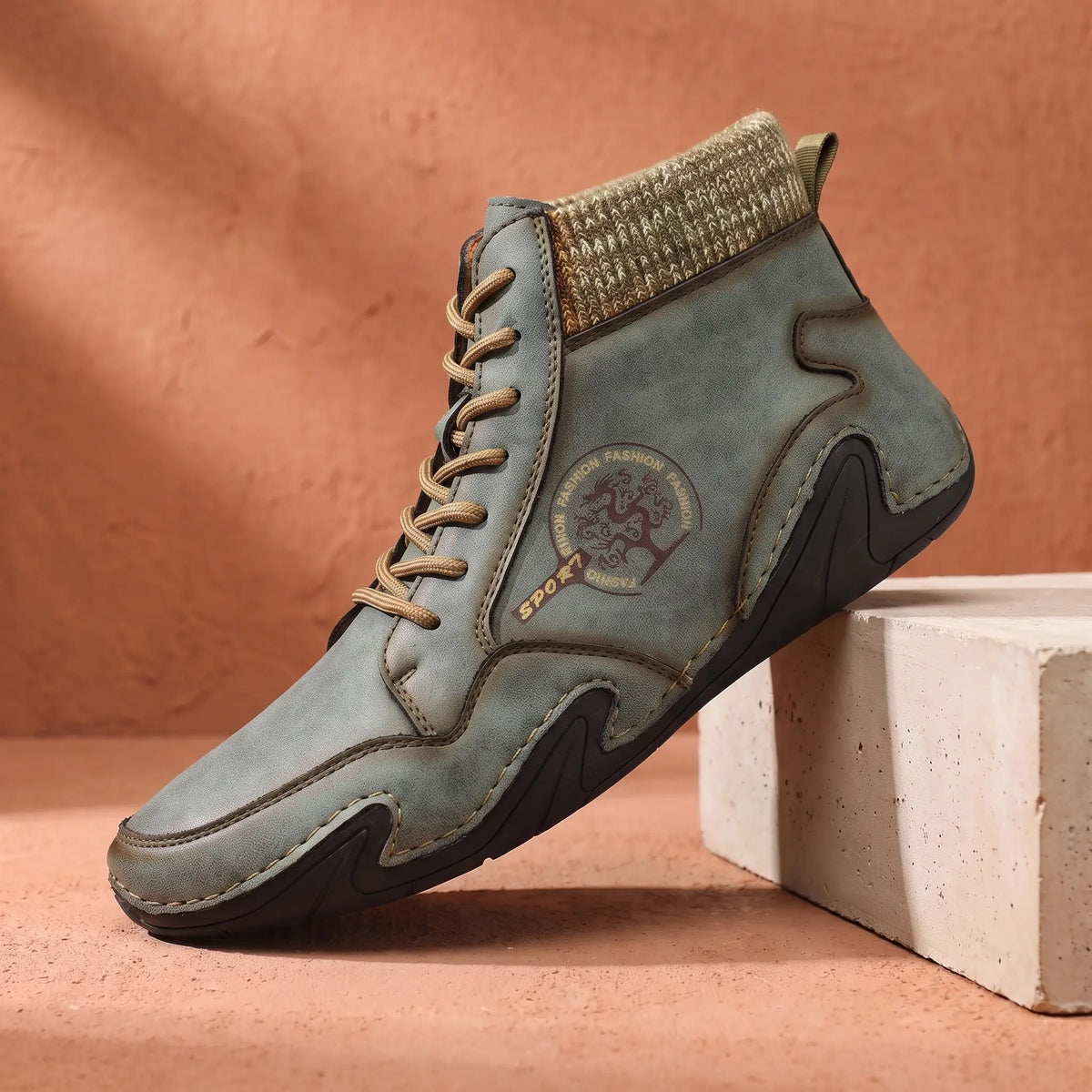 Men's green stitched leather ankle boot with knit collar on a concrete plinth
