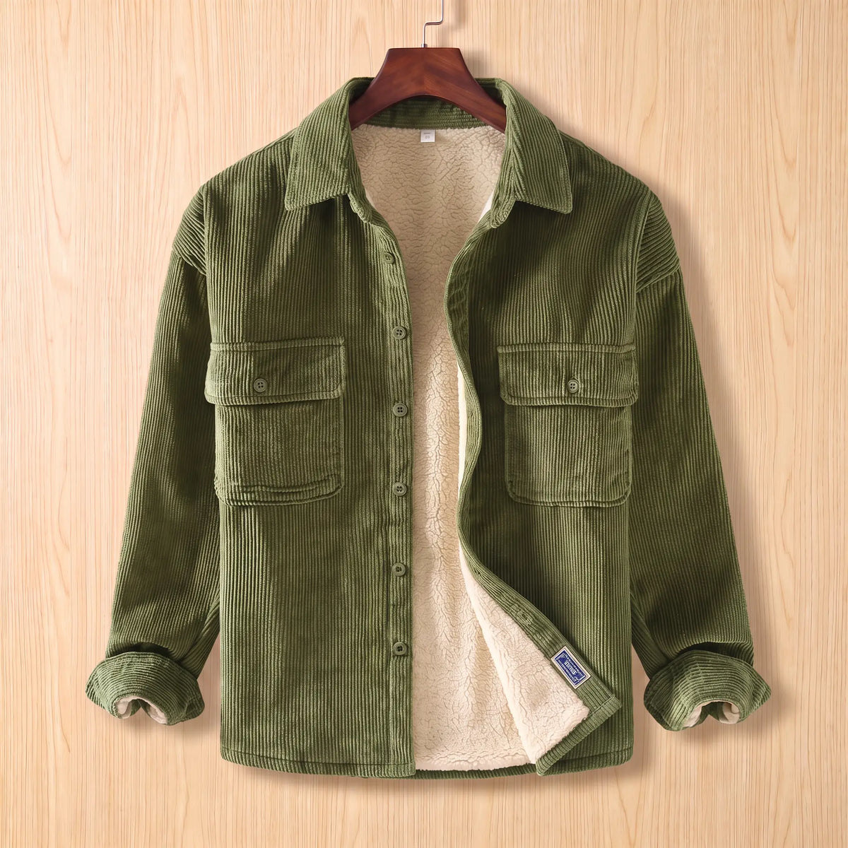 Layering Shirt Jacket in green, a fleece lined corduroy overshirt with two buttoned chest pockets on a wooden hanger