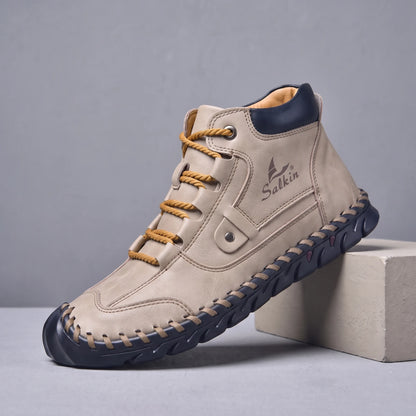 Beige hand-stitched men's lace-up ankle boot with navy sole, side view on a studio plinth