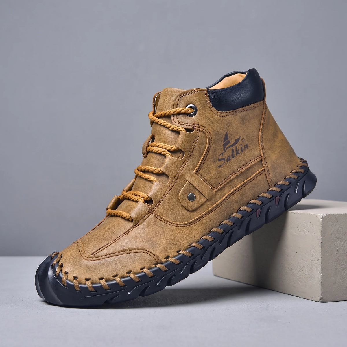 Brown hand-stitched men's lace-up ankle boot with navy sole, side view on a studio plinth