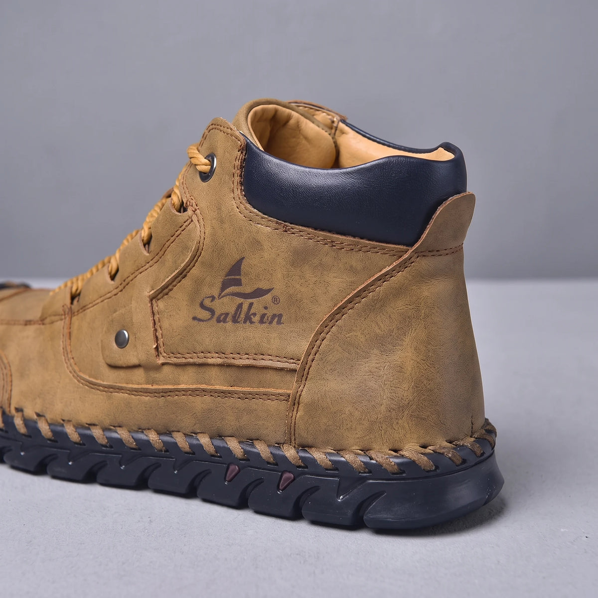 Close-up of the padded navy collar and stitched sole edge on the brown men's ankle boot