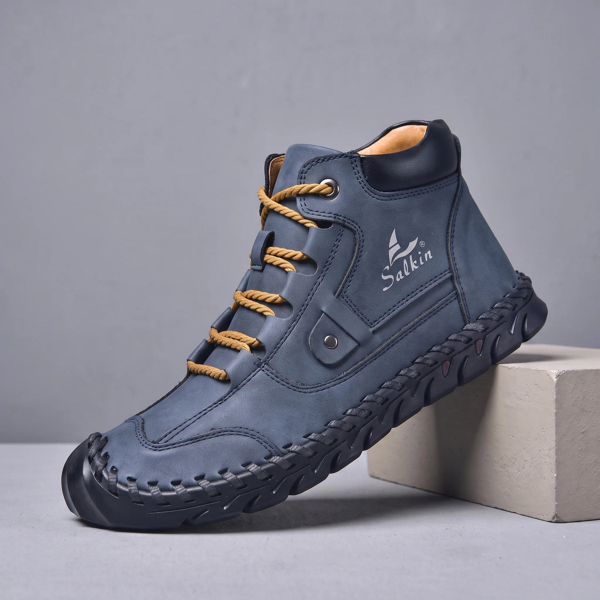 Navy hand-stitched men's lace-up ankle boot with navy sole, side view on a studio plinth