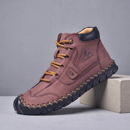 Red hand-stitched men's lace-up ankle boot with navy sole, side view on a studio plinth