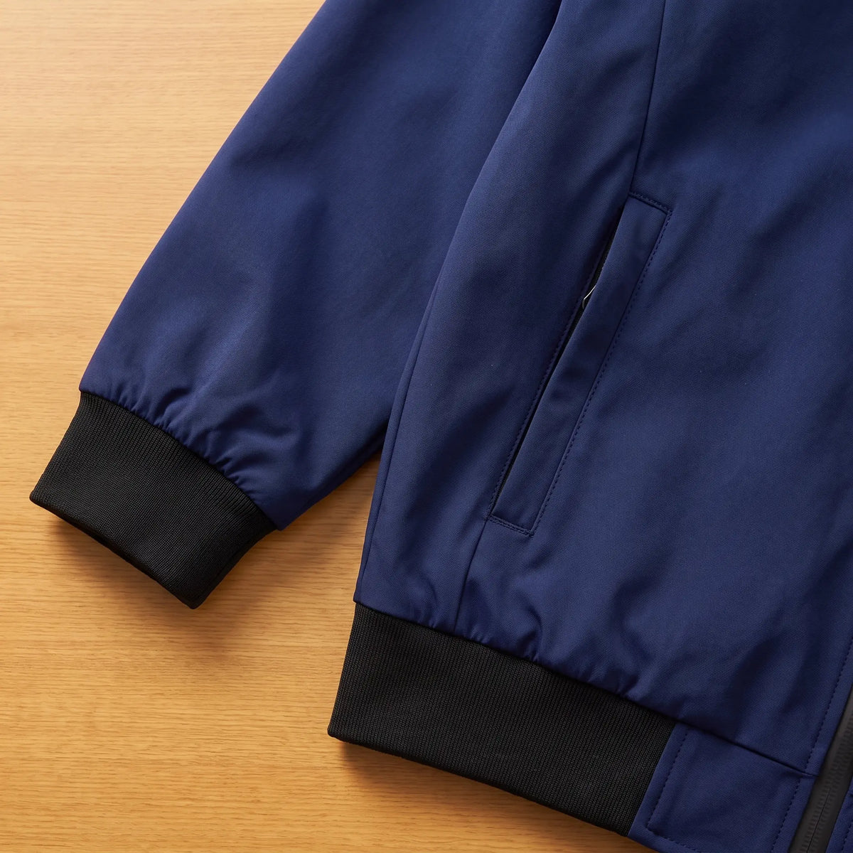 Close detail of MATTE SHELL BOMBER showing the ribbed cuff, zip pocket and hem