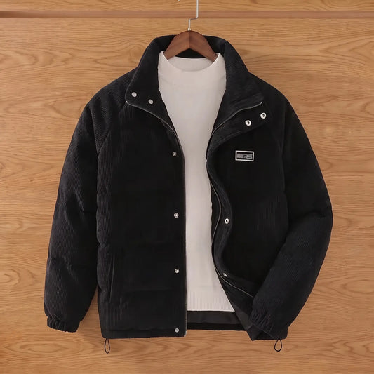 Black padded corduroy puffer jacket on a wooden hanger against an oak plank wall