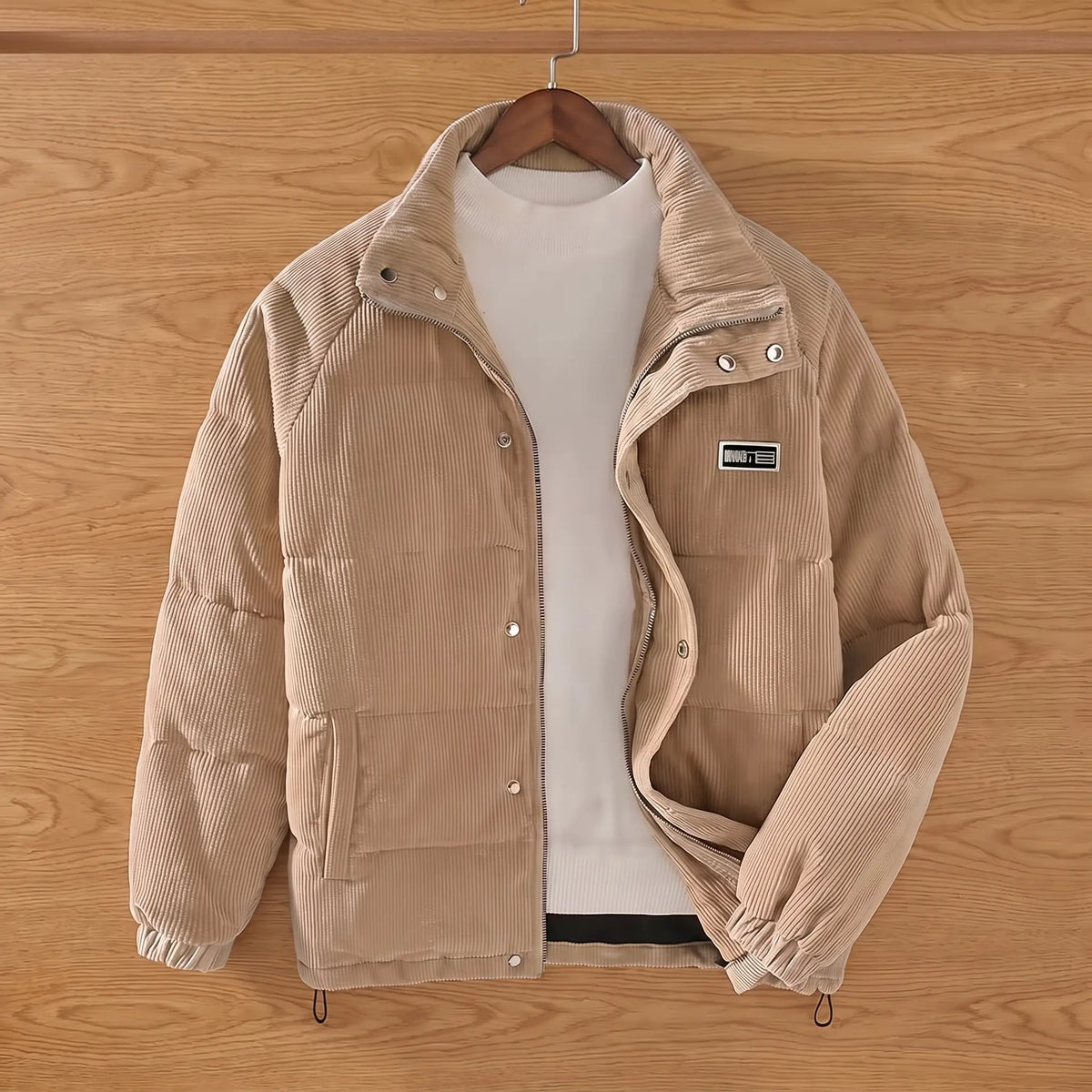 Khaki padded corduroy puffer jacket on a wooden hanger against an oak plank wall