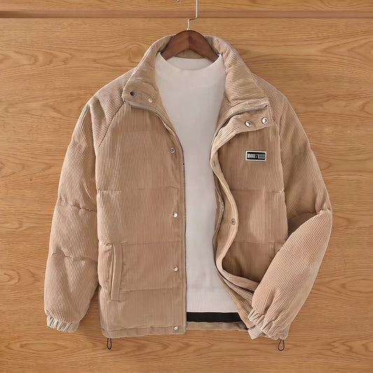 Khaki padded corduroy puffer jacket on a wooden hanger against an oak plank wall