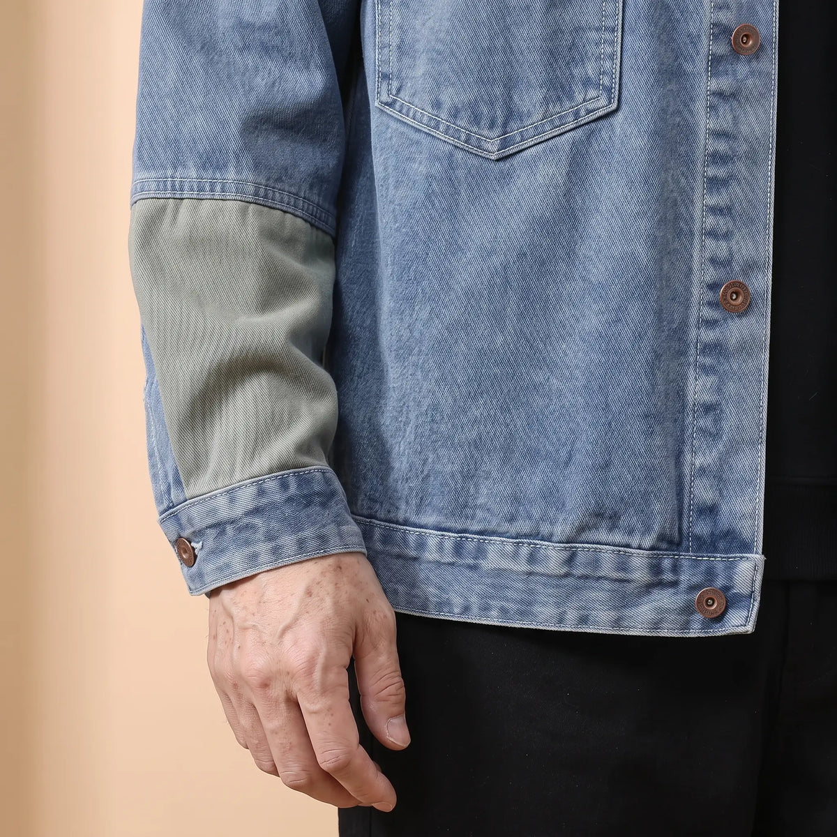 Close-up of the denim jacket buttoned cuff at the wrist with the hem tab and sage sleeve panel