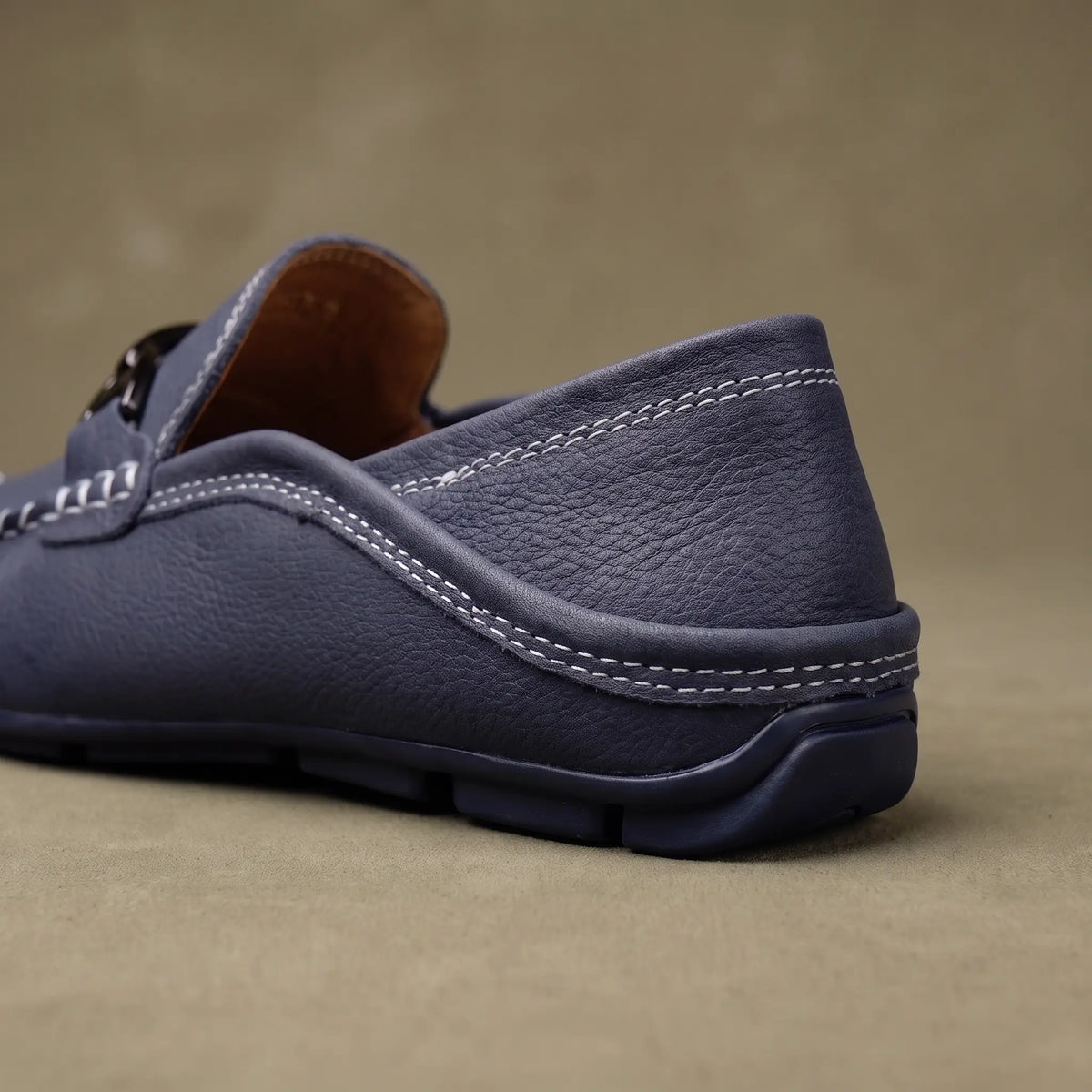 Close up of the padded collar welt stitching and flexible rubber sole on a blue leather driving loafer