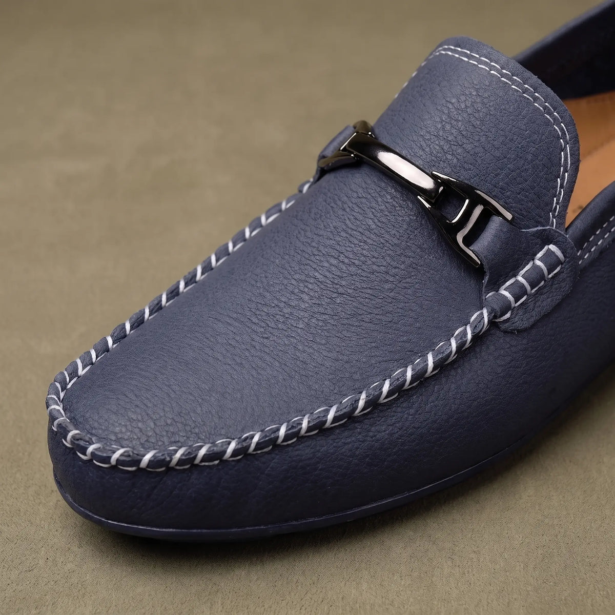 Close up of the silver metal bar and moccasin apron stitching on a blue leather driving loafer