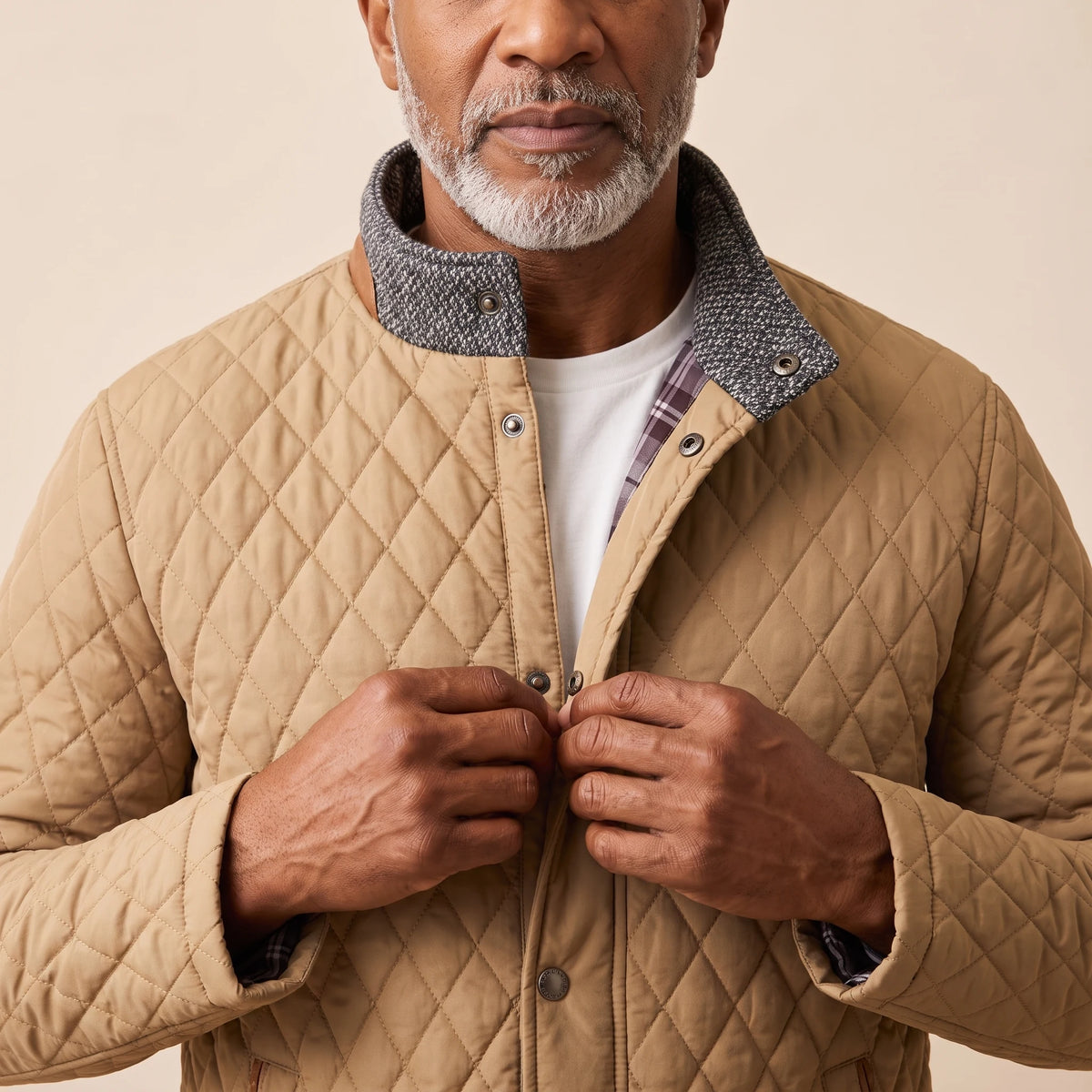 Man snapping the khaki quilted jacket closed over a white tee