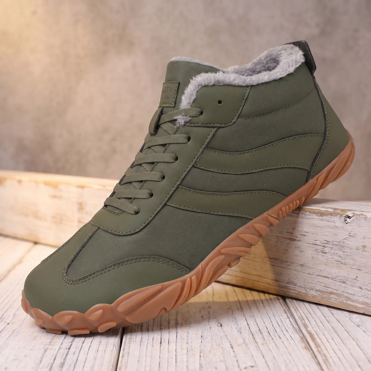 Men's green plush lined lace-up winter boot with gum tread sole on a pine ledge