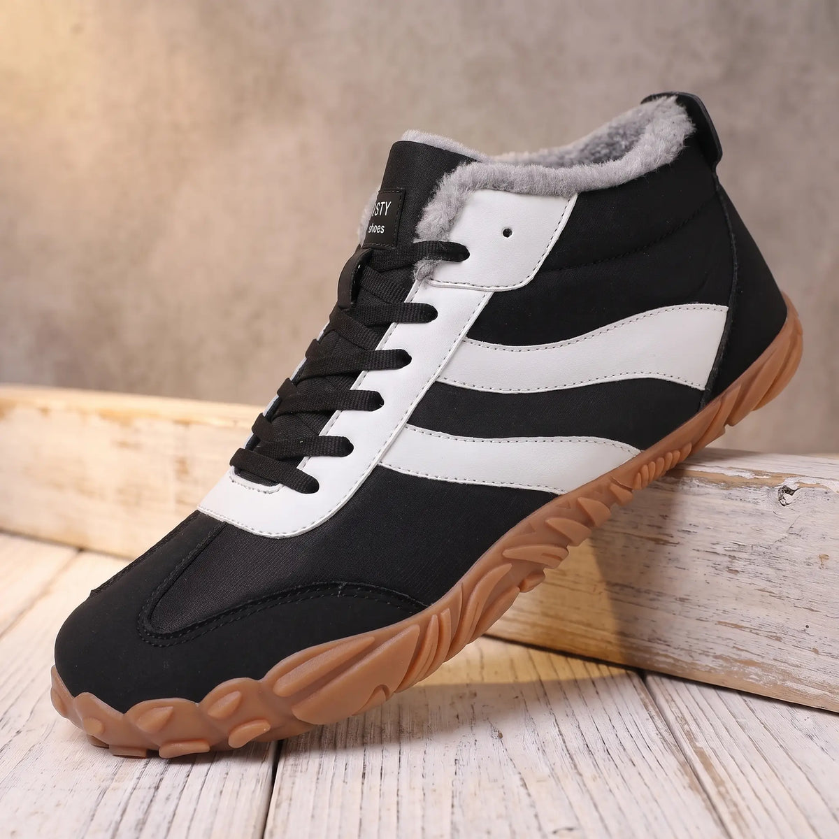 Men's black winter boot with white side stripes and plush collar on a pine ledge