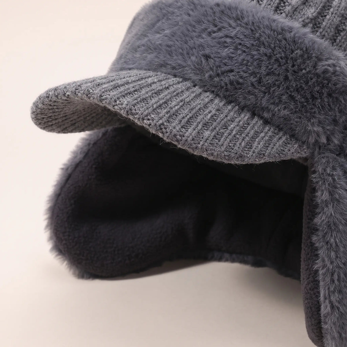 Close-up of grey earflap beanie showing knitted peak and dark fleece lining inside the ear flaps