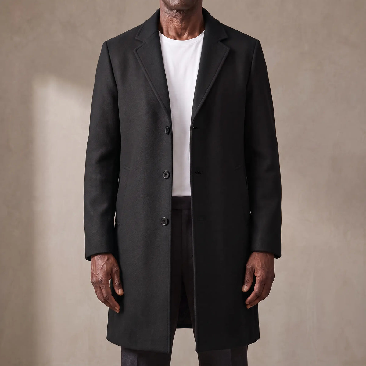 Black long wool overcoat with quilted lining worn open over a white tee