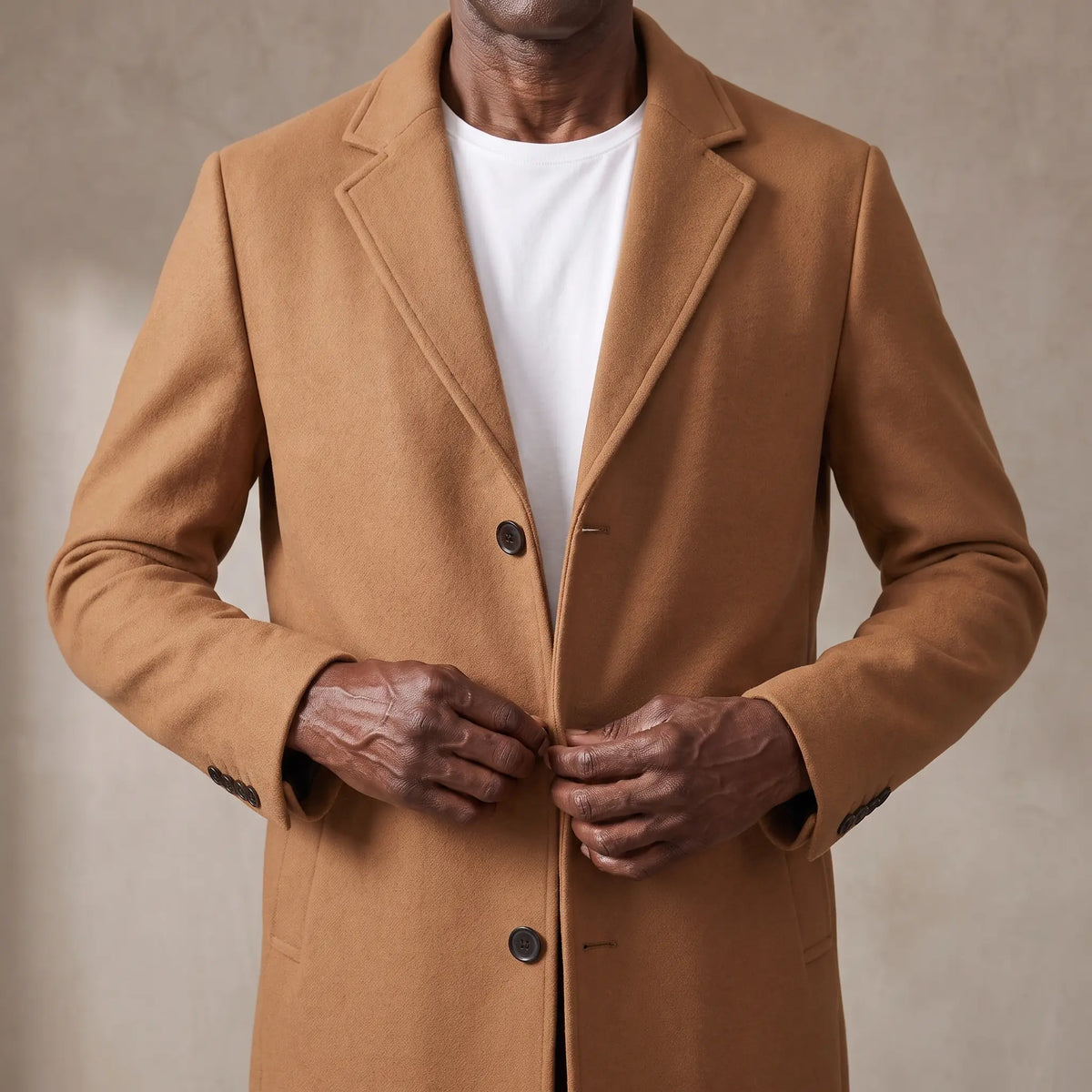 Man buttoning the tan wool overcoat at the chest