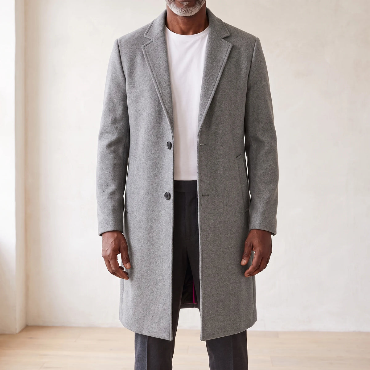 Grey knee-length men's overcoat with two-button front and quilted lining, worn open over a white tee