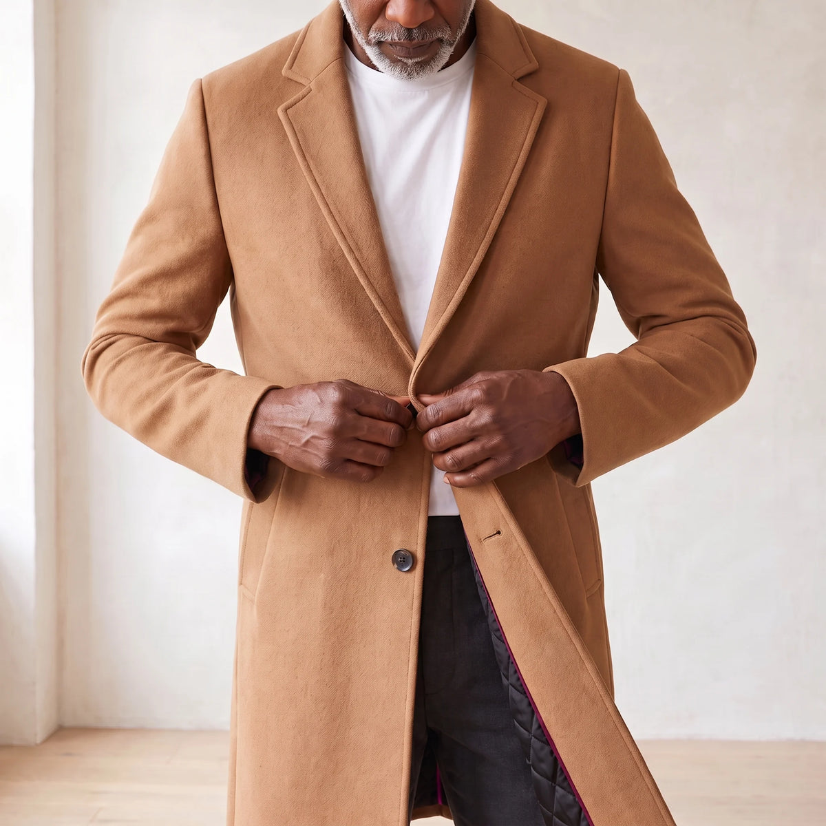 Man buttoning the tan knee-length quilted lining overcoat