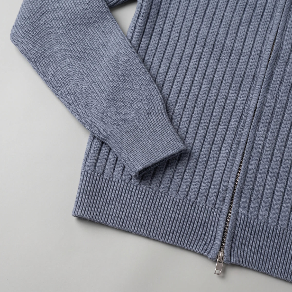 Ribbed cuff, vertical ribs and ribbed hem of the grey knit cardigan laid flat