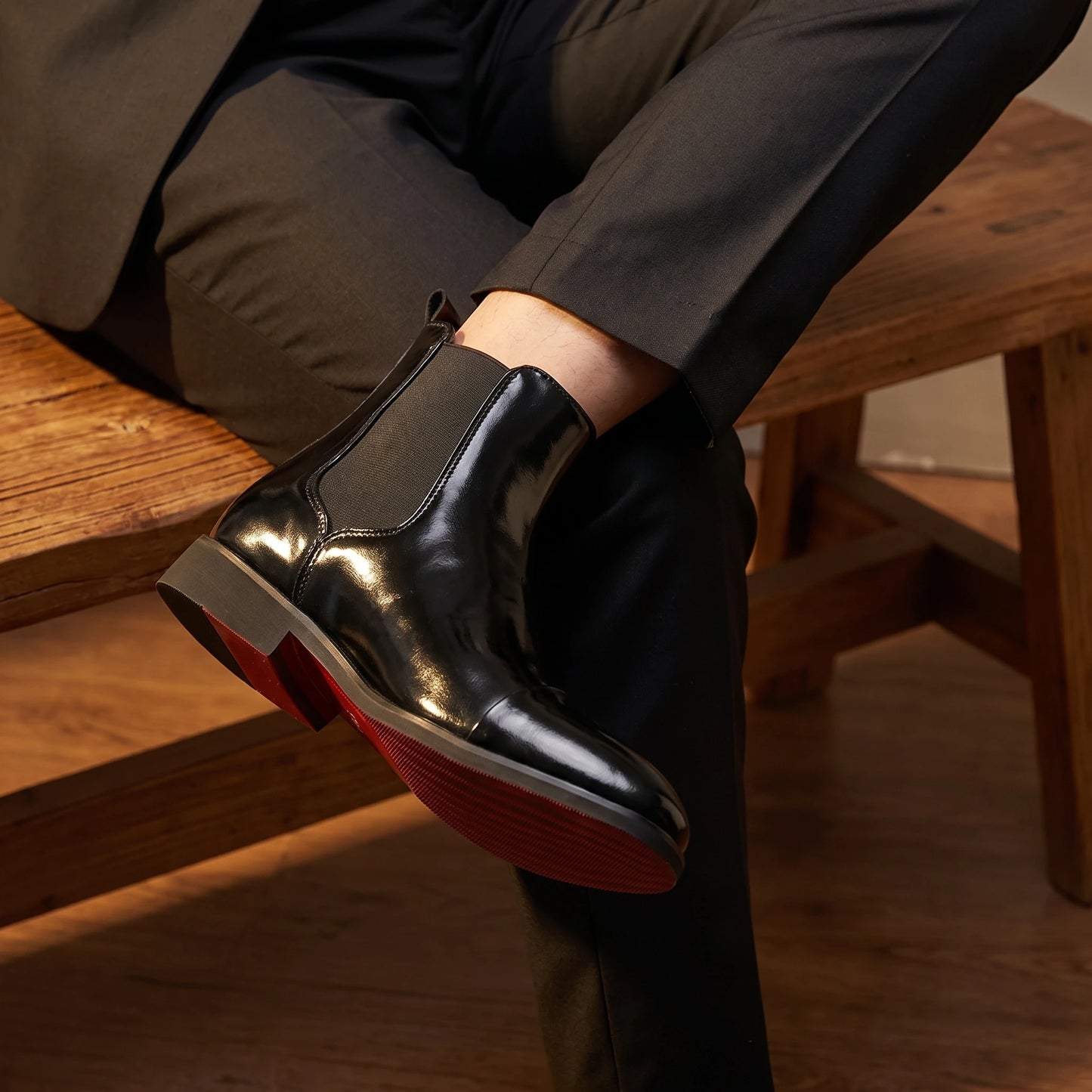 Man wearing RED SOLE BOOTS in black patent, seated with red sole showing
