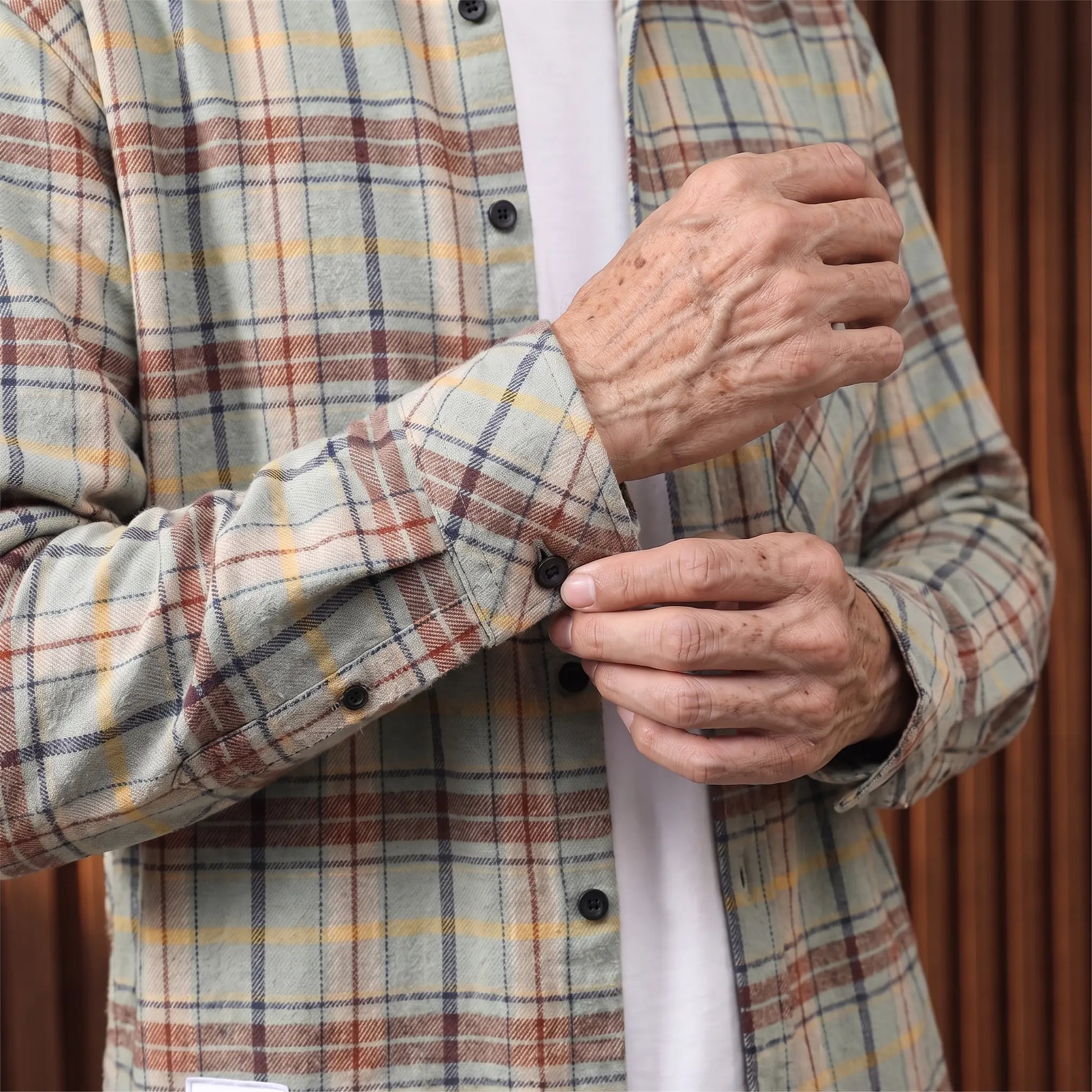 Older man fastening the cuff button on the plaid flannel shirt