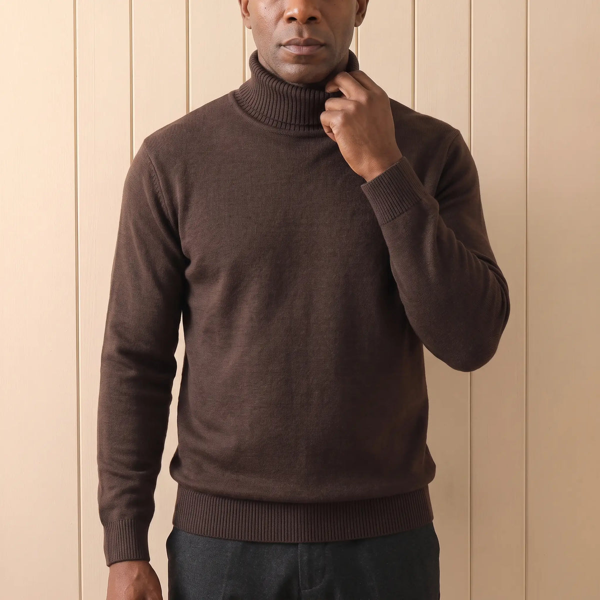 Man folding down the neck of a brown roll neck sweater