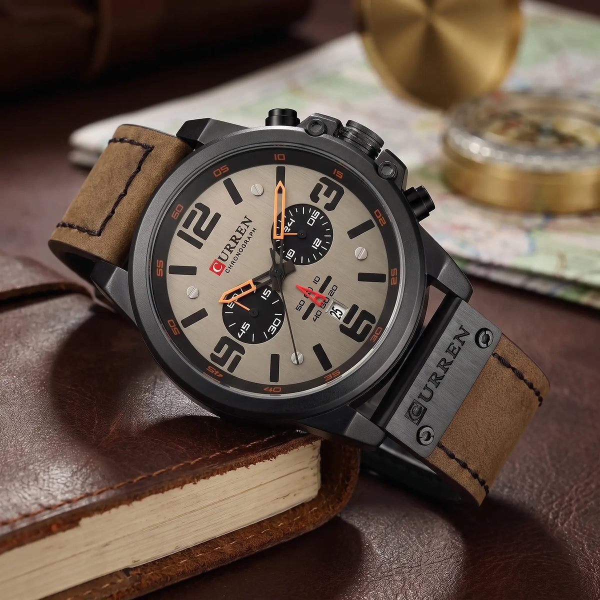 Black chronograph watch with grey dial and brown leather strap draped over a leather journal
